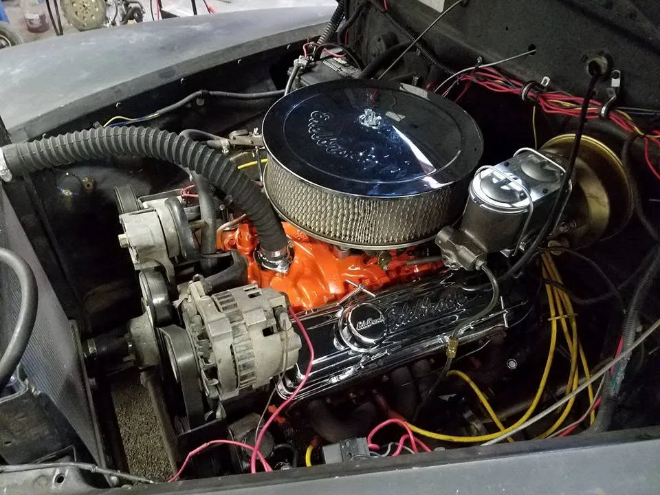 An orange small block engine mid-installation with a chrome air cleaner and new wiring run through the engine bay
