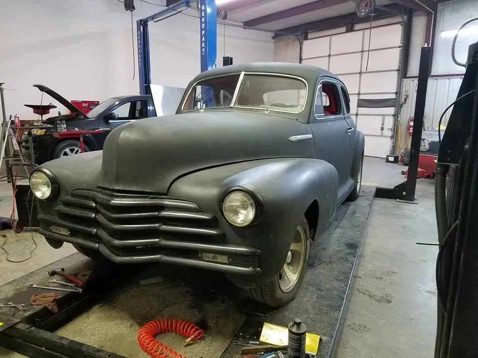 A late-1940s Chevrolet coupe in primer sitting on the lift inside the Armstrong Automotive shop